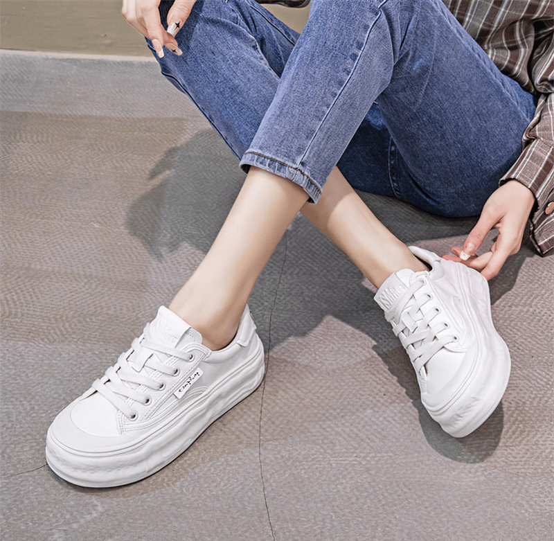 Woman wearing sports lace-up sneakers with thick sole, sitting cross-legged in jeans. Fashionable and comfy for active days.